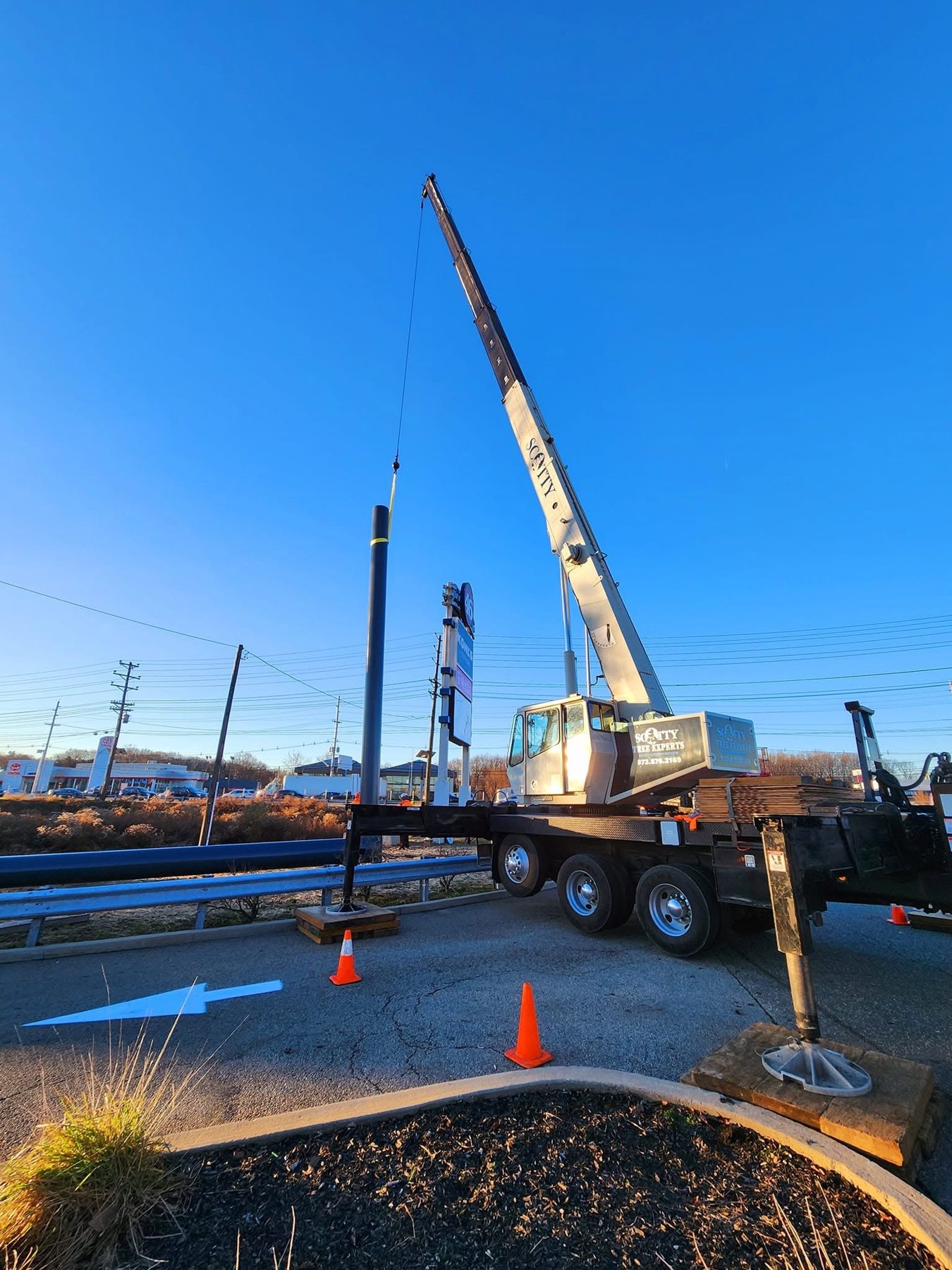 Scotty Tree Experts crane positioning a sign support beside a roadway